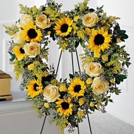 Heart-shaped floral wreath with yellow sunflowers and cream roses on a stand