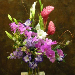 Tall mixed bouquet with pink orchids, white calla lilies, and purple blooms in a glass vase