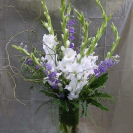 Tall white and purple floral arrangement in a glass vase