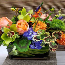 Mixed floral arrangement in a rectangular glass vase with orange and pink blooms