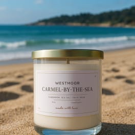 A scented candle in a glass jar with a gold lid on a sandy beach