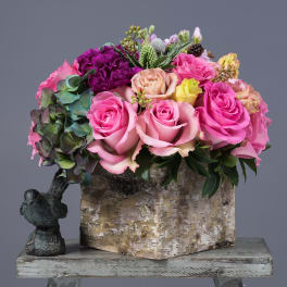 Pink and purple rose arrangement in a birch box with a small bird figurine