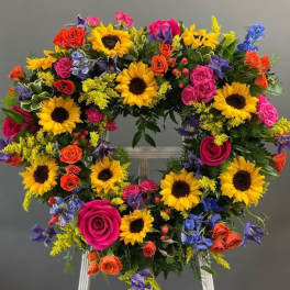 Heart-shaped floral wreath with sunflowers, roses, and blue accents on an easel