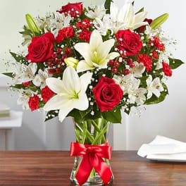 Red roses and white lilies in a clear vase with a red ribbon