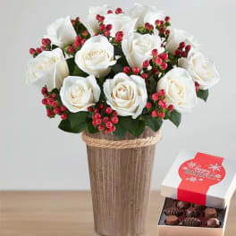 White roses in a tall vase with a box of chocolates beside it