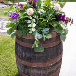 Purple and white floral arrangement in a wooden barrel
