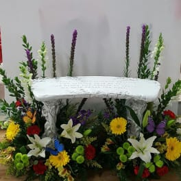 White memorial bench surrounded by colorful flowers and butterfly decorations