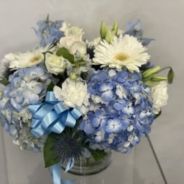 Blue and white bouquet with hydrangeas, gerbera daisies, and a blue ribbon in a glass vase