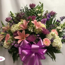 Large bouquet of pink lilies, purple flowers, and white hydrangeas with a purple bow