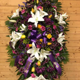 Large standing floral spray with white lilies, purple and pink flowers, and a purple ribbon