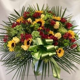 Large floral spray with sunflowers, red blooms, and a green ribbon bow