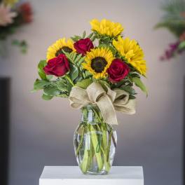 Bouquet of red roses and yellow sunflowers in a glass vase with a burlap bow