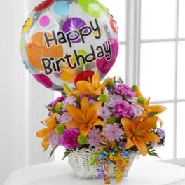 Birthday balloon above a basket of orange lilies and mixed flowers