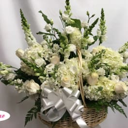 White floral arrangement in a wicker basket with a silver bow
