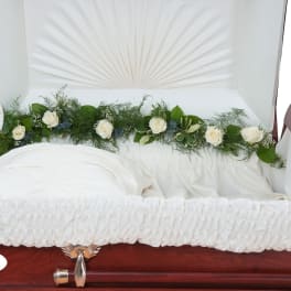 White roses and greenery arranged inside an open casket