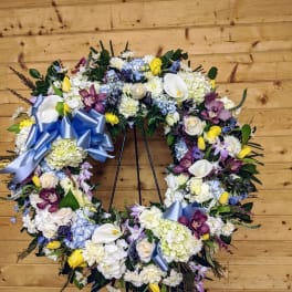 Large floral wreath with mixed blooms and blue ribbon on a stand