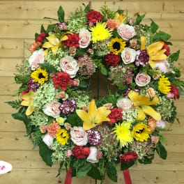 Large circular floral wreath with mixed roses, lilies, and sunflowers