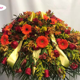 Large floral spray with red roses and orange gerbera daisies, accented by yellow ribbons