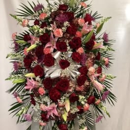 Large standing floral spray with red roses, pink lilies, and a white ribbon bow