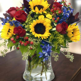 Bouquet of sunflowers, red roses, and blue flowers in a glass vase