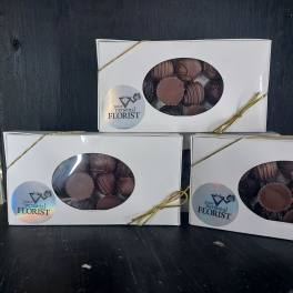 Three white window boxes of assorted chocolates tied with gold cord on a dark surface