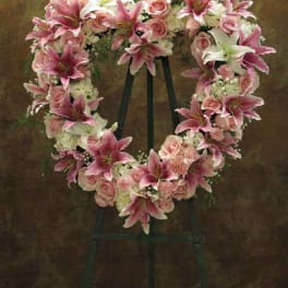 Heart-shaped floral wreath with pink lilies and roses on an easel