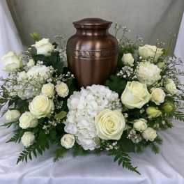 White roses and hydrangeas arranged around a bronze urn.
