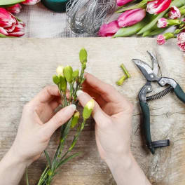 Hands arranging pink tulips and carnations with floral shears on a work surface