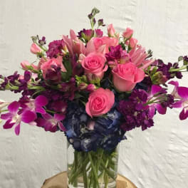 Pink roses and purple flowers arranged in a clear glass vase