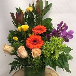 Mixed bouquet in a green vase with orange gerberas, roses, and purple orchids