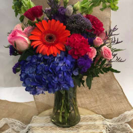 Colorful mixed bouquet in a glass vase with hydrangeas, roses, and a gerbera daisy