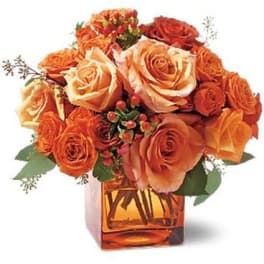 Orange and peach roses arranged in a square amber vase