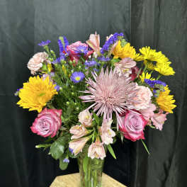 Mixed bouquet of pink, yellow, and purple flowers in a glass vase