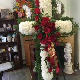 Large funeral cross of white flowers and red roses with a ribbon