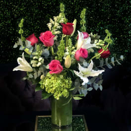 Bouquet of pink and red roses with white lilies in a tall glass vase