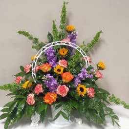 Colorful floral arrangement with sunflowers, roses, carnations, and purple blooms in a white basket