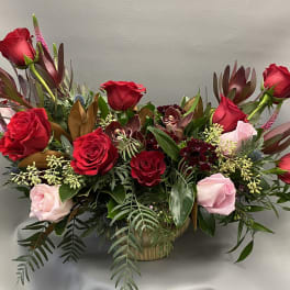Red and pink roses arranged in a low basket with mixed foliage