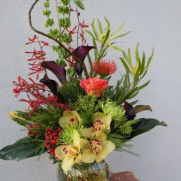 Tall tropical flower arrangement in a glass vase with orchids and calla lilies