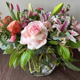 Mixed bouquet of pink roses, lilies, and tulips in a glass vase