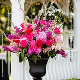 Tall pink and red floral arrangement in a dark urn on a pedestal