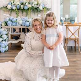 Bride and young girl in white dresses posing before blue and white floral decor