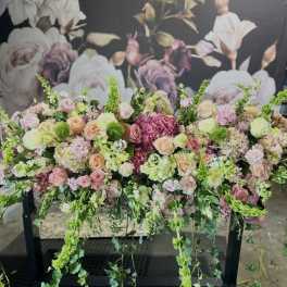 Large pastel floral arrangement with cascading greenery on a black stand