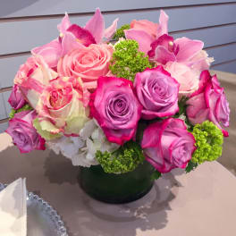 Pink and purple roses with orchids in a low vase