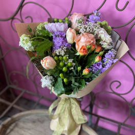 Mixed bouquet of pink, purple, and white flowers wrapped in brown paper