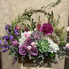 Garden-style arrangement of purple roses, succulents and white hydrangeas in a wooden box.
