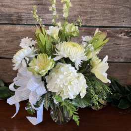 White floral arrangement in a clear glass vase with a white ribbon