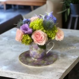 Small bouquet of pink and purple flowers in a floral teacup on a matching saucer