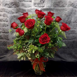 Red roses arranged in a clear glass vase with a red ribbon
