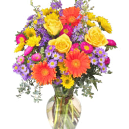 Colorful bouquet of yellow roses, orange gerberas, and purple daisies in a glass vase