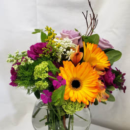 Mixed bouquet with orange gerbera daisies and lavender roses in a glass vase